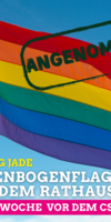 Obere Hälfte des Bilds eine wehende Regenbogenflagge, untere Hälfte Regenbogenflagge vor dem Kreishaus